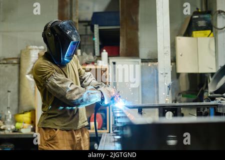 Welder in mask using torch to cut iron at his workplace in workshop Stock Photo