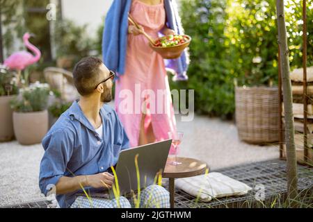 Happy young family with laptop and healthy lunch at backyard Stock Photo