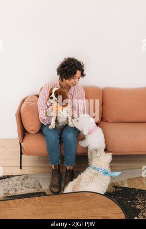 Young woman sitting on sofa with her three dogs Stock Photo