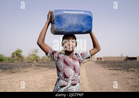 Young African girl carrying a heavy water container on her head, symbolising traditional roles of women in society blocking access to education, equal Stock Photo