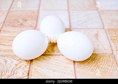 Three chicken bird eggs on a wooden pink orange checkered surface Stock Photo