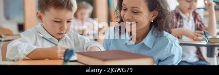 Happy kind teacher is helping a boy in elementary school lessons Stock Photo