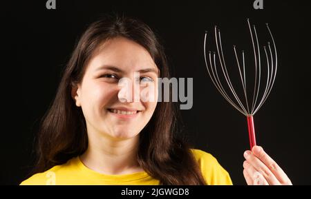 A woman with a metal flexible massager for self-massage of the head on a black background. Stock Photo