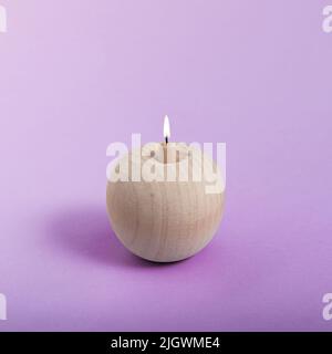 A wooden apple like a burning candle on a purple background. Minimal abstract summer concept. Isometric square layout. Stock Photo