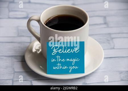 Motivational and inspirational quotes on blue note pad with coffee cup - Believe in the magic within you. Stock Photo