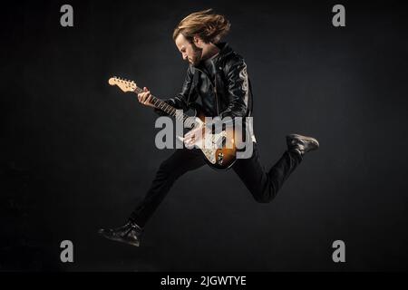 emotional bearded rock musician playing electric guitar in leather jacket and jumping, bas-guitar Stock Photo
