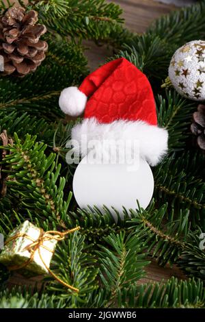 Santa Claus made from Christmas round white tag mockup wearing Santa hat on natural fir tree branch, with cones and Christmas decoration, Christmas sa Stock Photo