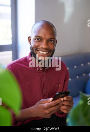 An attractive Black man smiles at the camera while using his phone Stock Photo
