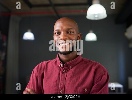 A confident happy Black man poses in red shirt in an industrial office Stock Photo