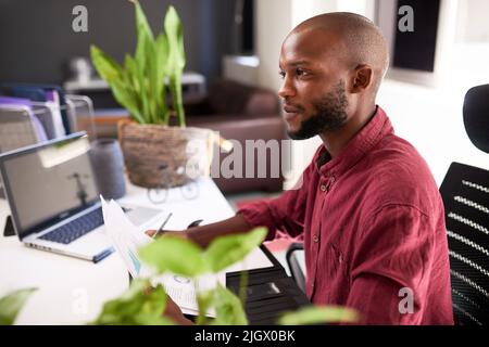 A Black man sits at his office desk with notes and laptop Stock Photo