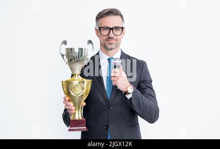 smiling mature man in suit hold champion cup and microphone isolated on white background Stock Photo