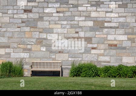 outdoor wooden bench near a large rock wall and shrubs and grass Stock Photo