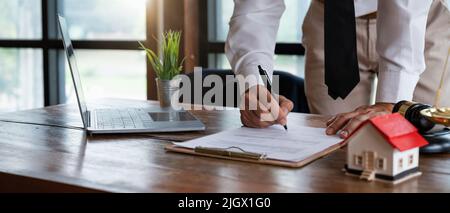 Close up young businessman standing near table with pen in hands, ready signing profitable offer agreement after checking contract terms of conditions Stock Photo