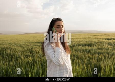 Female farmer, young female farmer standing near her wheat field and speaking to phone. Caucasian modern business woman working on farm. Stock Photo