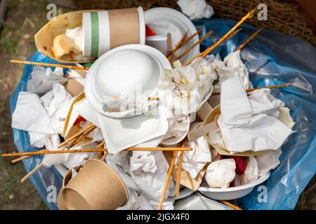 Close-up view of full garbage bin can with used dirty paper cardboard craft reusable sustainable cup, plates, towel napkins and cutlery at outdoor Stock Photo