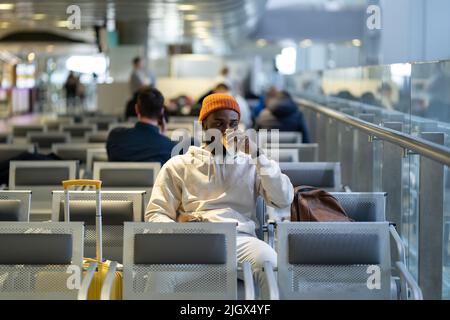 Young African man drinking coffee and eating sandwich while waiting for flying at airport terminal Stock Photo