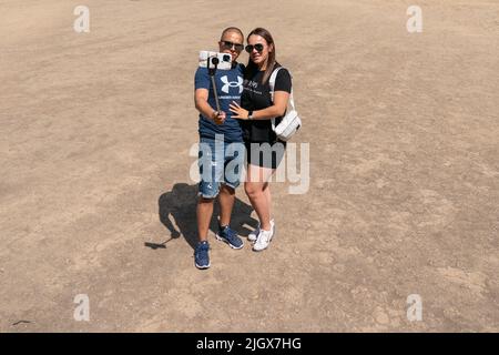 A couple pose for a selfie on the dried-up grass in Parliament Square, in Westminster, London, as the recent spell of hot weather continues, with the possibility of record temperatures early next week. Picture date: Wednesday July 13, 2022. Stock Photo