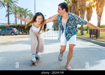 Young diverse couple with skateboard and longboard having fun outdoors. Stock Photo