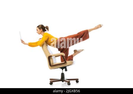 Portrait of young pretty girl, office worker in stylish attire dancing on armchair isolated over white studio background. Concept of beauty, business Stock Photo