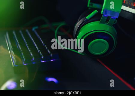 Computer gaming mouse and keyboard with purple backlight next to green headphones Stock Photo