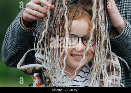 Female hands putting dreads over cute cute girl's. She is smiling, looking at the camera. Wearing glasses. Stock Photo