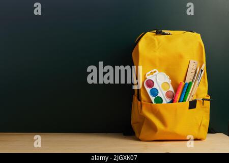 School backpack with colorful school supplies on table. Stock Photo