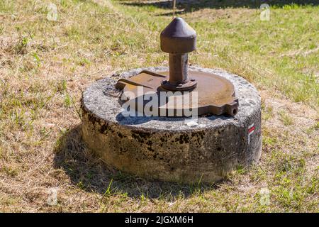 A rusty metal cap on a round concrete base marks a capped spring beside the hiking trail on the Rocher du Vellan plateau near Die, France. The surrounding grass has already dried out in the summer heat. Stock Photo