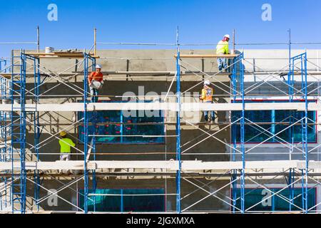 Four construction workers on scaffolding installing stucco to the outside of a commercial building between corner beading Stock Photo