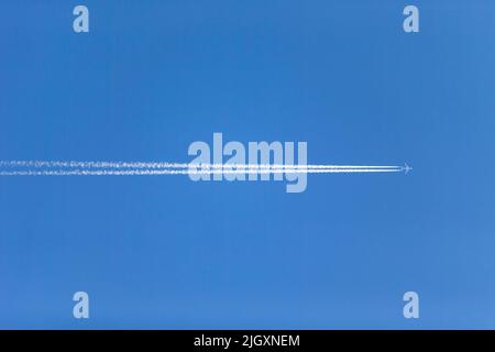 Large aircraft or plane flying overhead leaving contrails in the blue sky overhead. Stock Photo