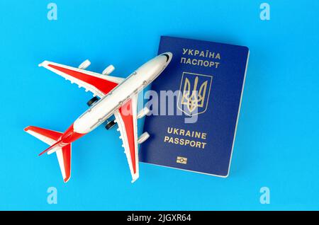 Ukrainian biometric passport and toy plastic plane on a blue background. Departure of Ukrainians abroad Stock Photo