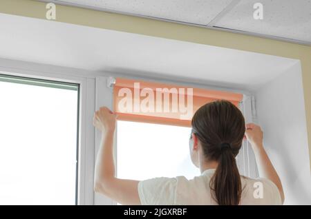 Installation of roller blinds. Woman specialist installs roller blinds on the window Stock Photo