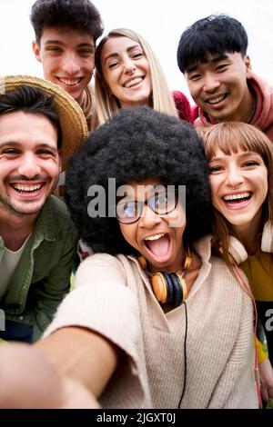 Vertical photo of Cheerful group of friends taking smiling selfie. Group of young people having fun together outdoors at park in the city enjoying Stock Photo