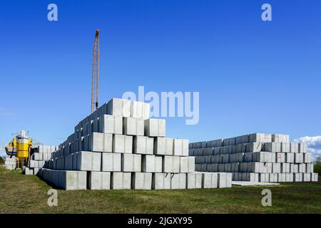 Stack of many large white concrete cube shaped blocks and yellow crane boom in the factory yard Stock Photo