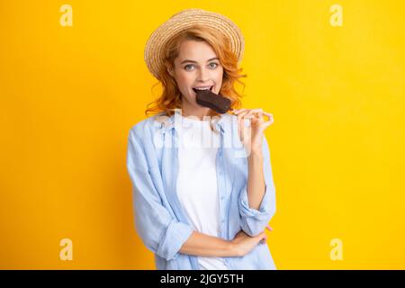 Portrait of cheerful funny teenage girl enjoys eating cold frozen dessert, eats delicious chocolate ice cream, yellow background. Stock Photo