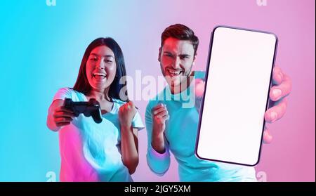 Cool App. Excited multiethnic gamer couple showing blank smartphone at camera Stock Photo
