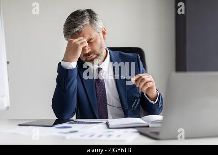 Overworking Concept. Tired Mature Businessman Suffering Headache During Work In Office Stock Photo