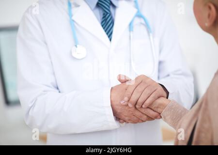 Close-up of unrecognizable male doctor in lab coat standing and holding hand of patient while supporting her Stock Photo