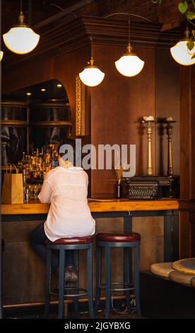 Beautiful woman is ordering a drink at the bar, view from the back. Drinking and waiting. Long-haired curly woman drinking wine and waiting for her ma Stock Photo