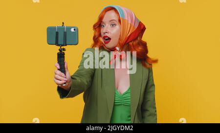 Wow reaction. Impressed redhead woman blogger taking selfie mobile phone selfie stick, communicating video call online with subscribers. Young girl ginger isolated alone on beige studio background Stock Photo - Alamy