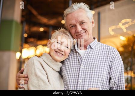 Portrait of positive beautiful elderly spouses in casual outfits hugging each other in modern cafe Stock Photo