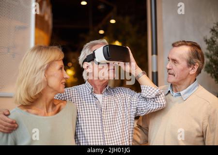 Curious senior man adjusting virtual reality goggles and embracing wife while entering world of virtual reality Stock Photo