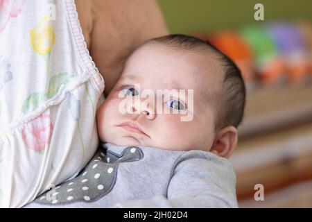 Zoomed in portrait of a beautiful one month old baby girl, held in bosom of grandparent against a colorful blurry background with room for copy. Stock Photo