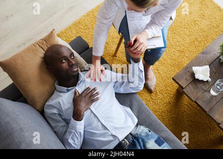 High angle view of serious young Afro-American man in shirt lying on sofa and feeling support of therapist Stock Photo