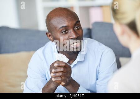 Bald young black man holding napkin in hands and talking to therapist while looking for solution Stock Photo