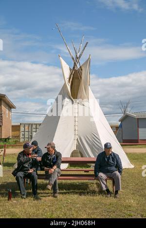 Indigenous Dene elder men sitting on picnic table outside of teepee in northern community of Deline, Northwest Territories, Canada Stock Photo