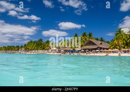 People sunbathing on the white sand beach with umbrellas, bungalow bar and cocos palms, turquoise caribbean sea, Isla Mujeres island, Caribbean Sea, C Stock Photo