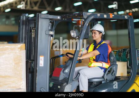 Asian beautiful woman driver drive fork lift car in industry with smile, ability of girl and diversity of career wearing helmet in reflective vest wor Stock Photo