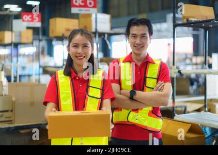 Young woman and man holding cardboard package working in warehouse among racks and shelves prepare for service moving delivering orders goods. Stock Photo