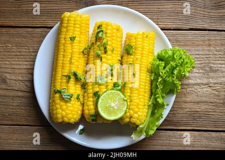 sweet corn cooked on white plate background, sweet corn food with salad vegetable lime coriander and lettuce, ripe corn cobs steamed or boiled sweetco Stock Photo