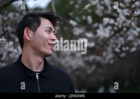 portrait of smiling Asian young man profile face with blur plum blossom flower tree Stock Photo